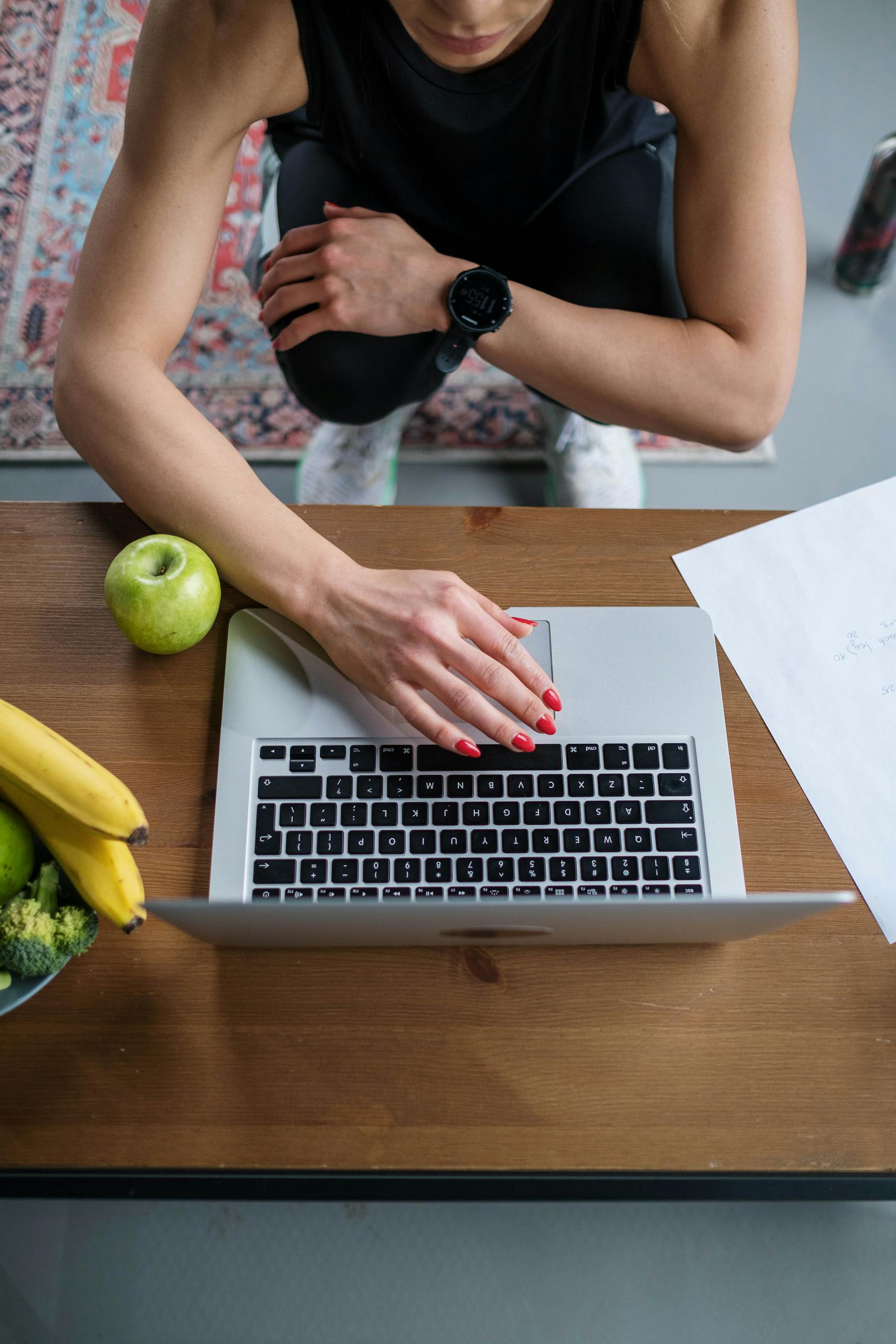 Overhead view of a woman using a laptop surrounded by fruits and documents.