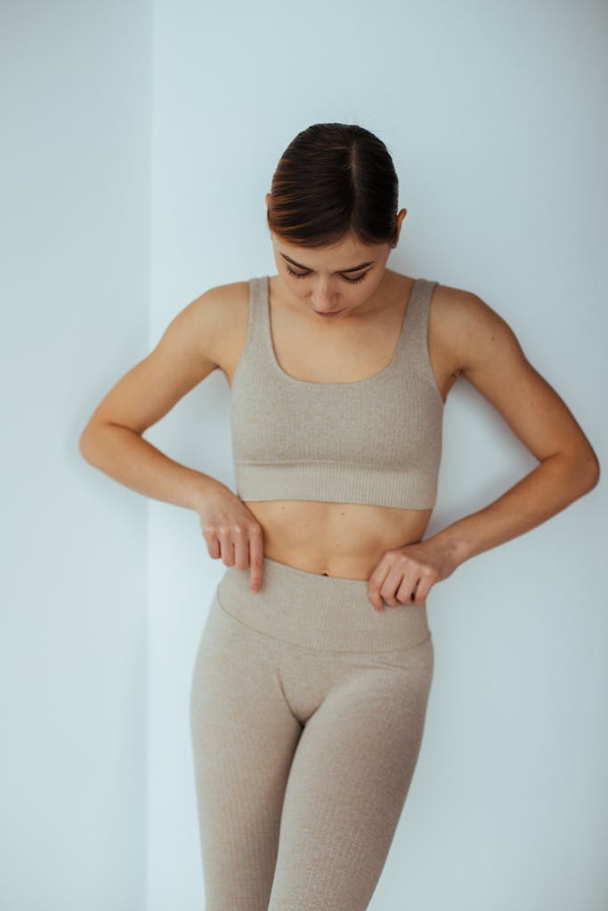 Young woman adjusting her fitted beige sportswear indoors for a modern fitness look.
